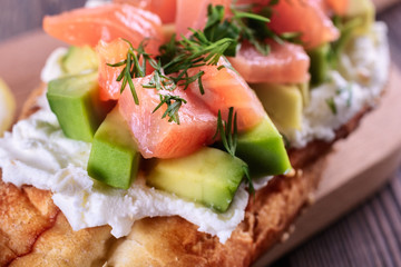 Delicious and healthy homemade sandwich with creamy cheese and slices of avocado and trout (salmon) are on a wooden board and ready to eat, macro