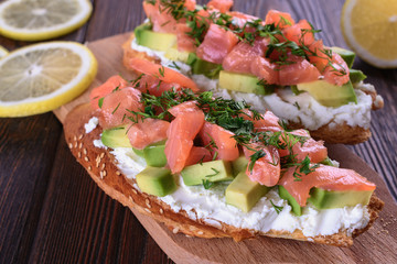 Delicious and healthy homemade sandwich with creamy cheese and slices of avocado and trout salmon are on a wooden board and ready to eat