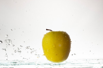 Green apple on a light background and splashing water