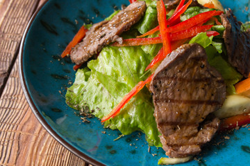 The salad with warm veal and oyster sauce in a plate on the wooden table.