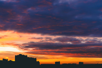 Cityscape with wonderful varicolored vivid fiery dawn. Amazing dramatic multicolored cloudy sky. Dark silhouettes of city buildings. Atmospheric background of sunrise in overcast weather. Copy space.