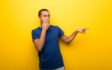 African american man with blue t-shirt on yellow background pointing finger to the side with a surprised face