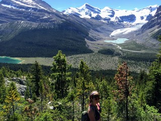 Naklejka premium A young female hiker resting along the Berg Lake trail in British Columbia, Canada. Mount Robson and Berg Lake are surrounded by forests and mountains in the background
