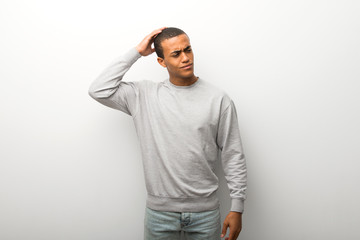 African american man on white wall background having doubts while scratching head