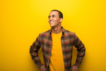 Young african american man on vibrant yellow background posing with arms at hip and laughing