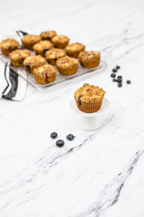 homemade blueberry muffins on wire rack on white and gray marble countertop; one isolated in front