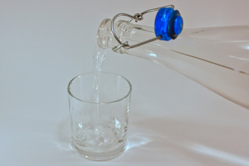 a clear bottle filling a empty glass with a clear liquid 