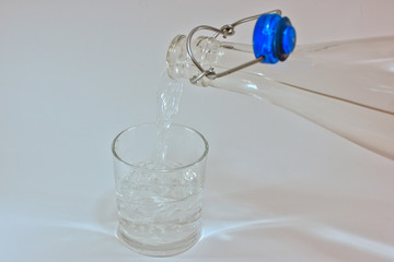 a clear bottle filling a glass with a clear liquid 