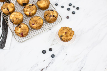 homemade blueberry muffins on wire rack on white and gray marble countertop; one isolated in front
