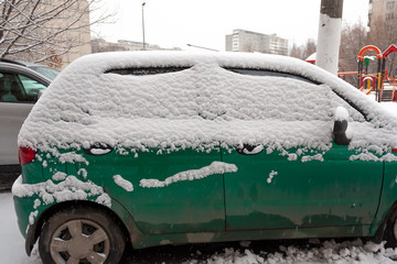 Dirty green compact car in the snow can not go. The first snowfall. cars covered in snow in the city. Transport problems, poorly clean snow.