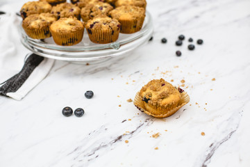 homemade blueberry muffins on cake pedestal on white and gray marble countertop; one isolated in front