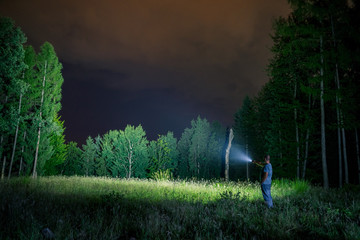 Man with flashlight in forest by night, explore - obrazy, fototapety, plakaty