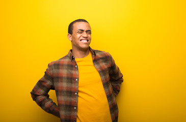 Young african american man on vibrant yellow background suffering from backache for having made an effort