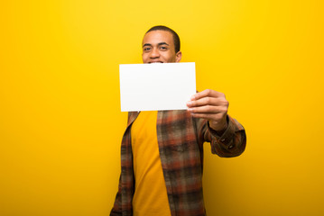 Young african american man on vibrant yellow background holding an empty white placard for insert a concept