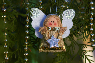 Festive decorations. Christmas angel on a tree branch. Gold beads. Handmade Christmas tree toy. Natural photo outdoors. Winter vacation. Happy New Year and Merry Christmas.