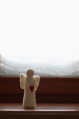 Woolen toy angel standing on a windowsill against a snowy window