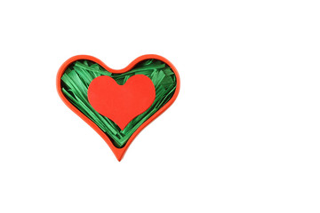 Red painted wooden heart enclosed with green paper raffia strips in red box isolated on white background