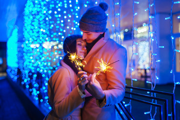 Young loving couple burning sparklers by holiday illumination