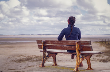 Lonely woman waiting on a bench at the beach.