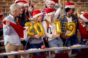Fototapeta na wymiar Smiling Students in Santa hat holding 2019 golden balloons at New Year party .