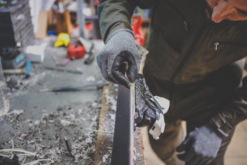 A man repairman in workshop ski service repairing the sliding surface of the ski at Ski vise. In...