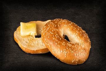 Fresh sesame seed bagel bread with a piece of melted butter, isolated on a black slate in background.