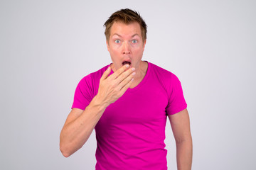 Young handsome man with purple shirt looking shocked while covering mouth