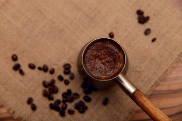 Coffee on the eastern cezve on a napkin of natural burlap background with scattered coffee beans. Horizontal, place for text, top view, abstract background.