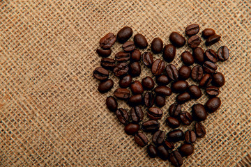 Coffee beans in the shape of a heart on a napkin of natural burlap background. Valentine's day concept. Horizontal, space for text, top view, abstract background.
