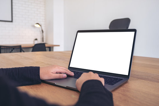 Mockup image of hands using and typing on laptop with blank white desktop screen on wooden table in office