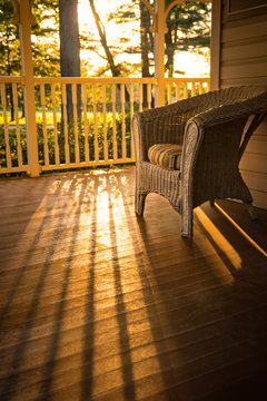 Warm sunny view of home: a wicker chair on wooden porch.