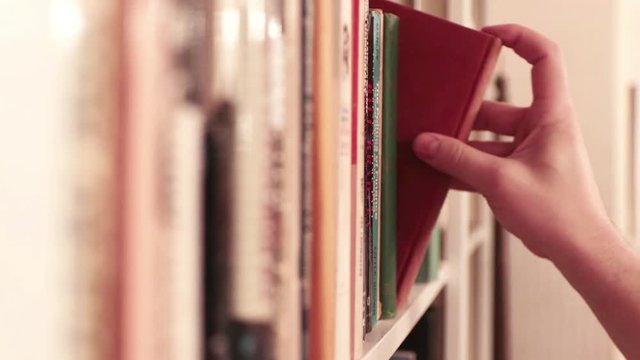 Hand reaches for and pulls classic book from library shelf; vintage look.