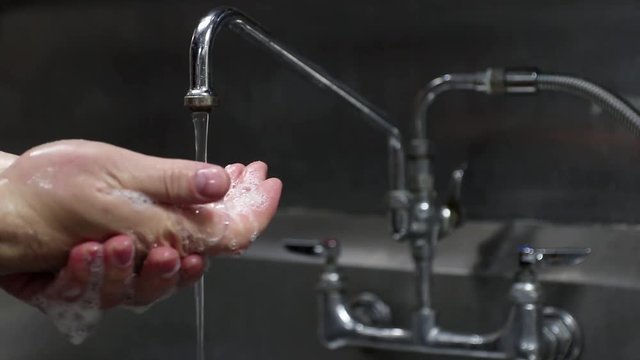Washing hands with soap and water in an industrial sink.	