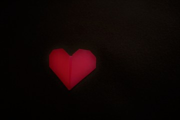 A red color origami heart on a black background