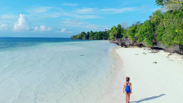 Aerial: woman walking on tropical beach, scenic turquoise water and white sand, Tomia Island, Wakatobi marine national park, Indonesia, paradise travel destination