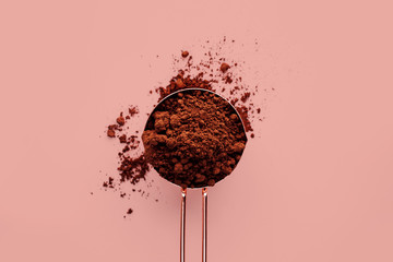 Rose gold measuring cup of cocoa powder on a pink background, healthy food concept