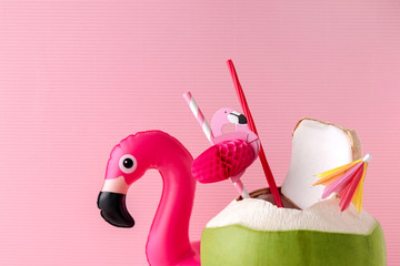 Fresh coconut on a pastel pink background with flamingo inflatable drink holder, summer vibes...