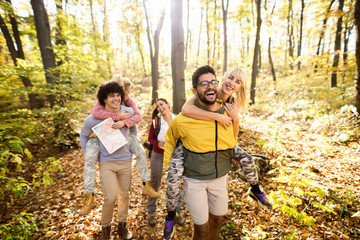 Couples having piggyback ride while walking through woods in autumn. Hiking concept.