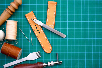 Handmade leather watch strap with pricking iron,stitching thread,burnish and slicker wooden in the leather workshop.Leather craft and DIY crafting tools on craftsman's work desk.Handmade ,DIY Concept.