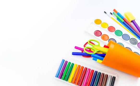 Pencils and felt-tip pens in a plastic cup, paints and pastel crayons on a white background