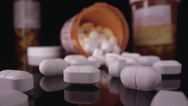 Prescription drugs, opioid painkillers in open bottle with camera moving across table top.