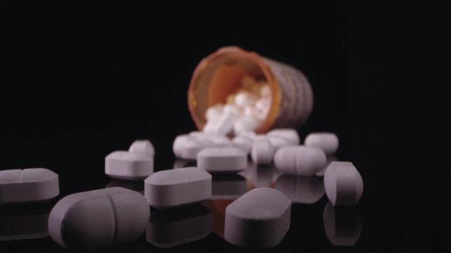 Opioids lying on black table top with open bottle moving into the bottle.