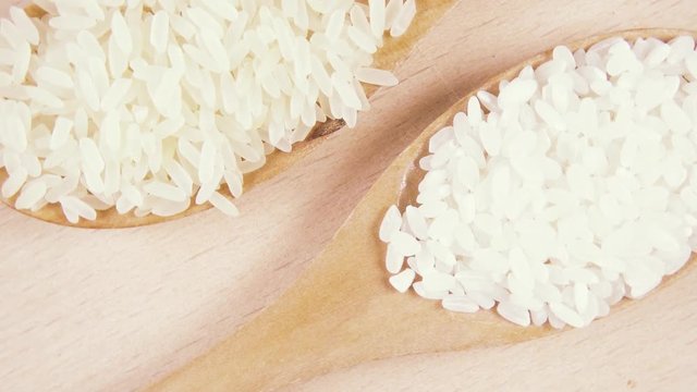 White long-grain and round-grain rice in wooden spoons on a wooden background rotate counterclockwise top view