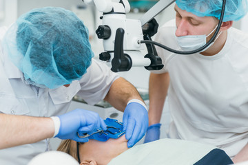 Doctor used microscope. Dentist is treating patient in modern dental office. Operation is carried out using cofferdam. Client is inserted and restored teeth, make denture. Orthodontist and assistant