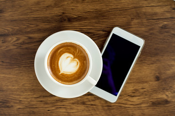 Fototapeta na wymiar Smart phone with latte art coffee on wooden background
