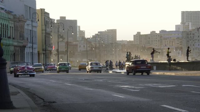 waves splash on cuban fishermen, old classic american cars driving on famous waterfront malecon promenade in Old Havana, Cuba