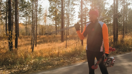 Training an athlete on the roller skaters. Biathlon ride on the roller skis with ski poles, in the helmet. Autumn workout. Roller sport. Adult man riding on skates.The athlete goes and holds sports