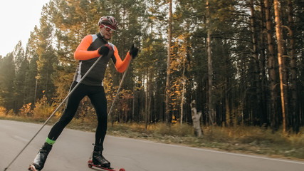 Training an athlete on the roller skaters. Biathlon ride on the roller skis with ski poles, in the helmet. Autumn workout. Roller sport. Adult man riding on skates. © ivandanru