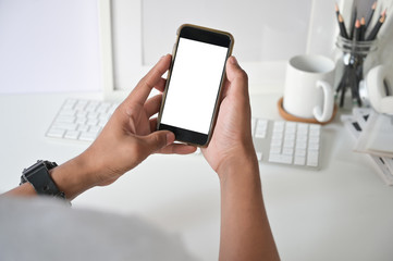 Mockup smartphone on man hands empty display with office desk background.