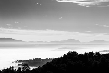 Fog filling a valley in Umbria (Italy), with layers of mountains and hills and trees in the foreground